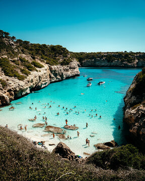 Mallorca, Spain - 15 September 2023: View of Cala des Moro with turquoise water, rocky cliffs, and people swimming and relaxing on the beach under a clear blue sky.