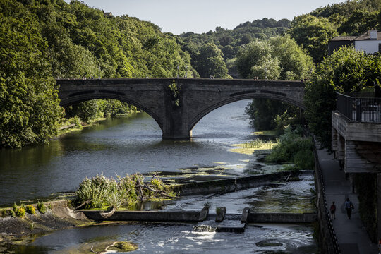 View of the historic stone bridge spanning the River Wear with lush green trees and a weir in the foreground in Durham, England, United Kingdom.