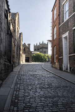 View of the historic cobblestone street leading towards the iconic Durham Cathedral, framed by traditional brick and stone buildings in Durham, England, United Kingdom.