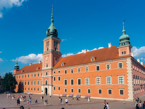 View of the historic Royal Castle in Warsaw Old Town with its pink facade and clock tower, set against a clear blue sky with people walking in the square, Warsaw, Masovian Voivodeship, Poland.
