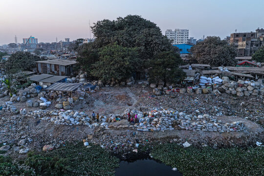 Aerial view of Buriganga River bank in Dhaka with workers sorting piles of white sacks near trees and urban buildings in Dhaka, Dhaka Division, Bangladesh.