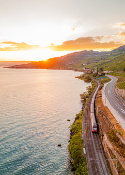 Aerial view of a train traveling along the tracks beside Lake Geneva with the terraced vineyards of Lavaux at sunset in Bourg-en-Lavaux, Vaud, Switzerland.