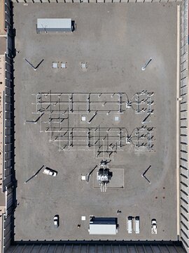 Aerial view of an electrical substation with power lines, transformers, and utility vehicles parked on a gravel lot in Thornton, Colorado, United States.