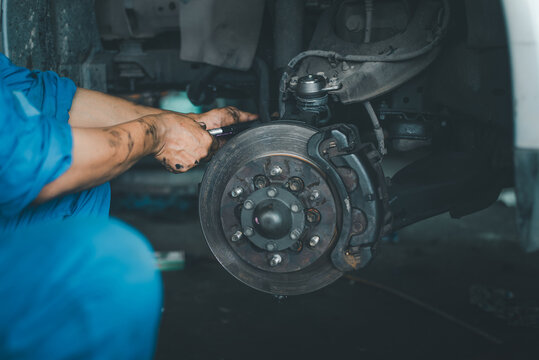 Auto repair technician fixing old vehicle wheel hub and disc brake with wrench, authentic photo, not AI.