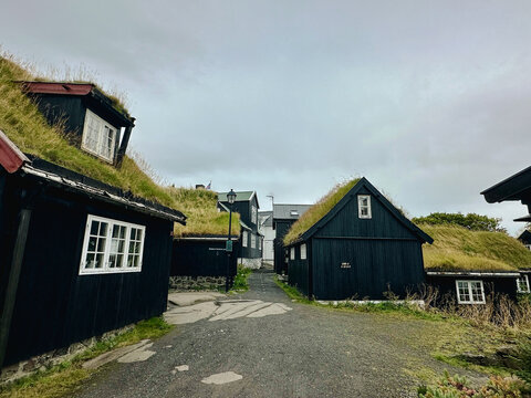 View of traditional black wooden houses with grass roofs lining a narrow gravel path in the Faroe Islands.