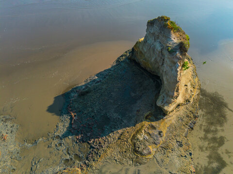 Aerial view of a unique coastal rock formation rising from the sandy beach with textured surfaces and shadows cast on the shore in Bali, Indonesia.