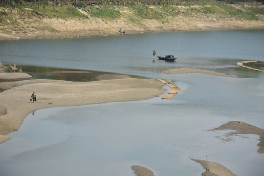 Kushtia District, Khulna Division, Bangladesh - 10 March 2020: View of a river with sandbanks, a small wooden boat, and a person walking along the shore.