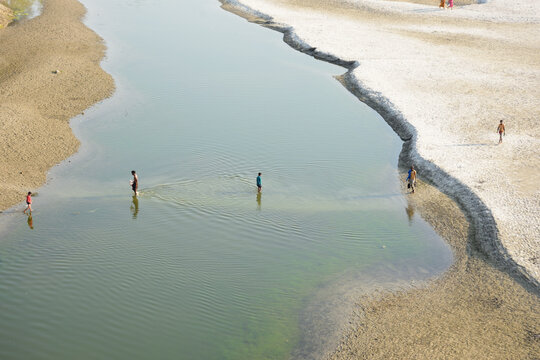 Kushtia District, Khulna Division, Bangladesh - 10 March 2020: View of people wading through the shallow waters of a calm river with sandy banks.