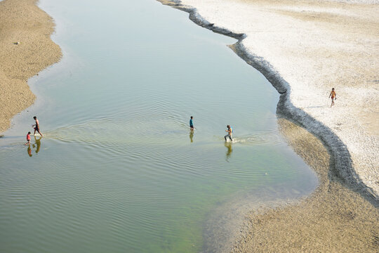 Kushtia District, Khulna Division, Bangladesh - 10 March 2020: View of people wading through the shallow waters of a calm river with sandy banks under clear daylight.