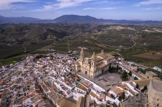 Aerial view of the Church of Our Lady of the Incarnation surrounded by white-washed houses, terracotta rooftops, and olive groves in Olvera, Andalusia, Spain.