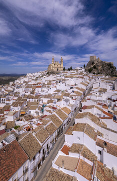 Aerial view of the white-washed town of Olvera with its historic church and castle perched on a hilltop under a bright blue sky in Olvera, Andalusia, Spain.