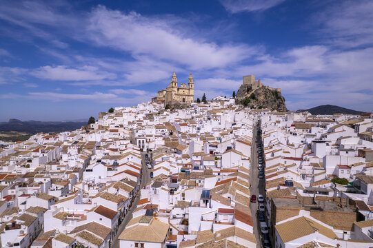 Aerial view of Olvera, a white village in Andalusia, featuring its hilltop church and castle overlooking dense traditional white houses under a blue sky. Olvera, Andalusia, Spain.