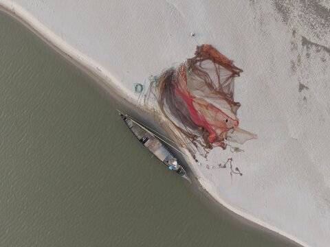 Aerial view of a wooden fishing boat moored on a sandy riverbank with large nets spread out to dry in Kushtia, Khulna Division, Bangladesh.