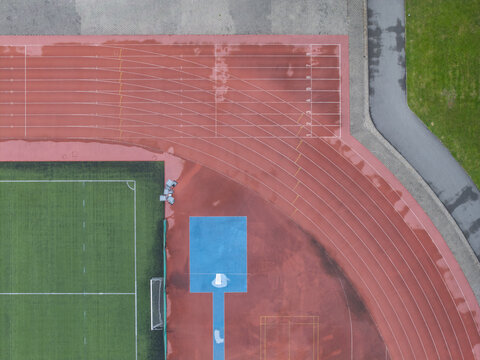 Aerial view of a wet running track and sports center with artificial turf and a blue long jump pit after rain in Wieliczka, Lesser Poland Voivodeship, Poland.