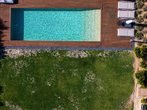 Aerial view of a rectangular swimming pool with turquoise water, wooden decking, lounge chairs, and a green lawn in Cascais, Lisboa, Portugal.