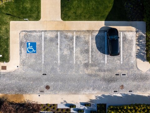 Aerial view of a handicap parking space and a black car parked in a cobblestone parking lot in Cascais, Lisboa, Portugal.