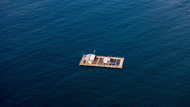 Aerial view of a floating fish farm platform on the calm blue waters of Pantai Karanggongso in Watulimo, East Java, Indonesia.