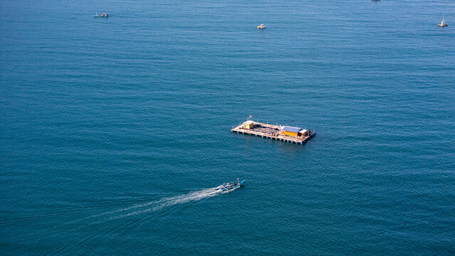 Aerial view of a floating fish farm platform on the calm blue waters of Pantai Karanggongso in Watulimo, East Java, Indonesia.