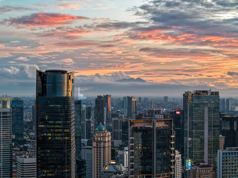 Aerial view of the Jalan Jendral Sudirman skyline with modern skyscrapers and glass towers under a dramatic sunset sky in Kecamatan Setiabudi, Daerah Khusus Ibukota, Indonesia.