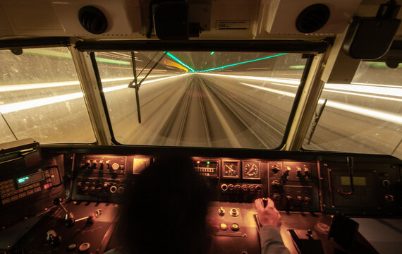 View of a train cockpit at night, with the driver's hand on the controls and light trails visible through the window while in a tunnel at Schiphol, Noord-Holland, Netherlands.