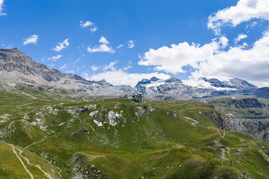 Aerial view of Breuil-Cervinia nestled in the green slopes of the Aosta Valley with snow-capped Alps and a glacier in the background under a blue sky, Breuil-Cervinia, Aosta Valley, Italy.
