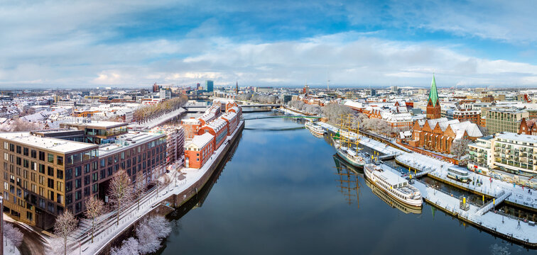 Aerial view of the Weser river featuring snow-covered rooftops, historic architecture, St. Martin's Church, and boats docked along the riverbank in Bremen, Germany.