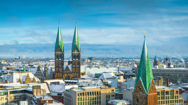 Aerial view of St. Peter's Cathedral with its distinctive green spires rising above the snow-covered rooftops of Bremen, Germany.