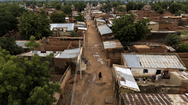 Aerial view of the town of Dambatta with its traditional mud houses, corrugated metal roofs, and a central dirt road lined with trees in Dambatta, Kano, Nigeria.