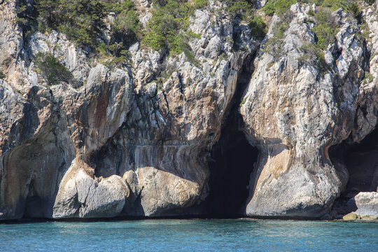 View of Gulf of Orosei with rugged limestone cliffs and a sea cave overlooking turquoise water in Italy.