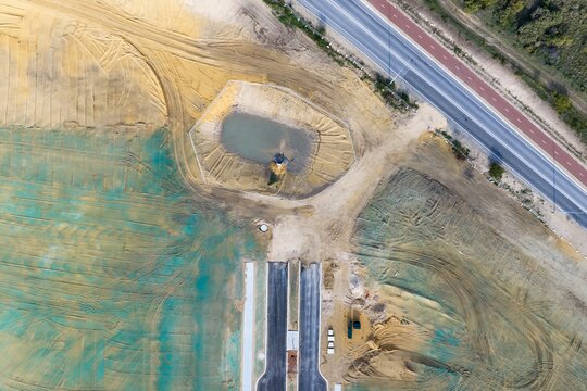 Aerial view of a residential development construction site with earthworks, a drainage pond, and new road infrastructure in Perth, Western Australia, Australia.