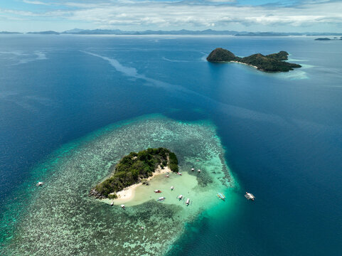 Aerial view of CYC Beach in Coron, featuring turquoise waters, coral reefs, and traditional outrigger boats anchored near the sandy shore, Coron, Mimaropa, Philippines.