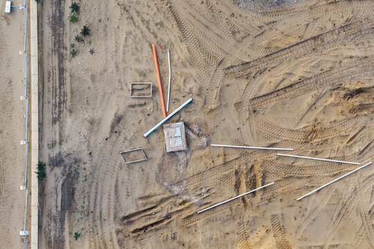Aerial view of a residential development site featuring exposed sandy ground, scattered construction pipes, and vehicle tire tracks in Perth, Western Australia, Australia.
