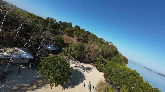 FPV aerial view of Pass Island with white sand beach and traditional outrigger boats in clear turquoise water in Culion, Mimaropa, Philippines.