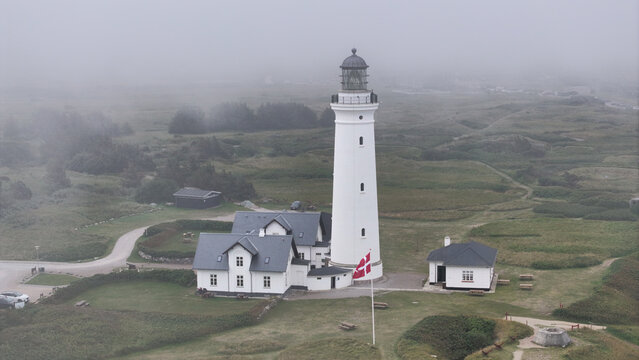 Aerial view of Hirtshals Fyr lighthouse standing amidst grassy dunes and foggy coastal landscape in Hirtshals, Denmark.
