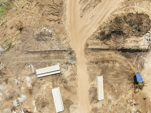 Aerial view of a construction site with dirt paths, piles of concrete materials, and a small structure covered by a blue tarp in Garut, West Java, Indonesia.