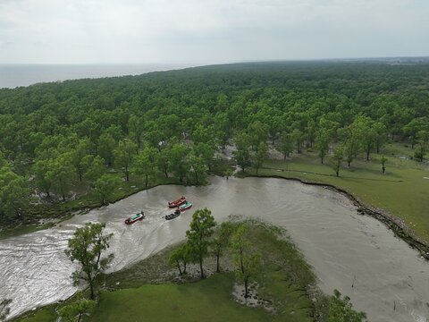 Aerial view of a winding river flowing through a lush green forest with small boats navigating the water in Sitakund, Chittagong Division, Bangladesh.