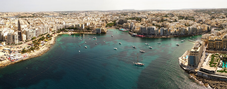 Aerial view of boats anchored in the turquoise waters of the bay, surrounded by dense urban architecture and coastal buildings in St Julian's Bay, Malta.