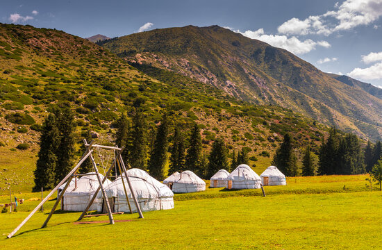 View of Kok Jaiyk valley with traditional yurts set in a lush green meadow, surrounded by majestic mountains under a blue sky in Dzhetyoguz, Issyk-Kul Region, Kyrgyzstan.