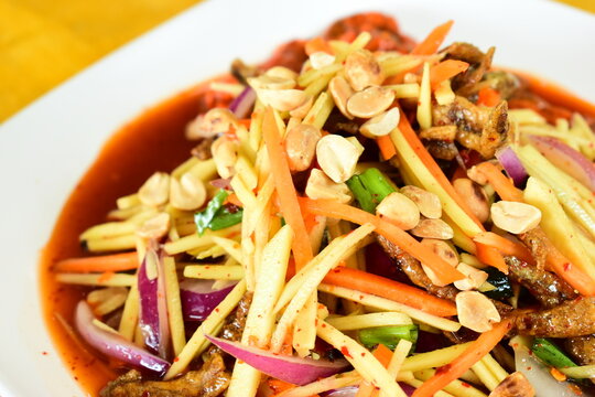 Thai spicy green mango salad serve on white plate, flavors of traditional Thai cuisine