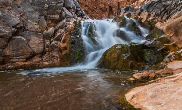View of the waterfall in Canon de Guatin with flowing water cascading over textured volcanic rocks in the arid landscape of San Pedro de Atacama, Antofagasta, Chile.