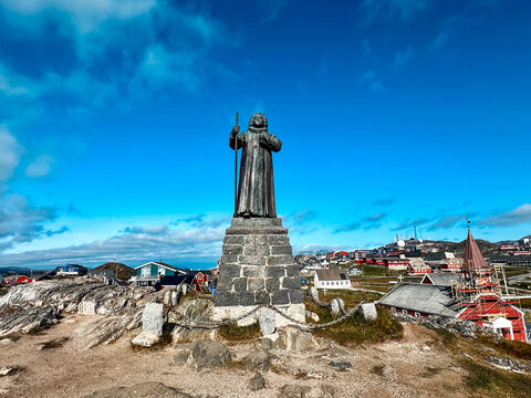 View of the Hans Egede Statue standing on a stone pedestal overlooking the colorful houses and coastal landscape of Nuuk, Greenland.