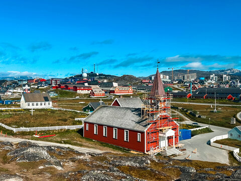 View of the Church of Our Saviour in Nuuk surrounded by colorful houses, rocky terrain, and clear blue sky in Greenland.