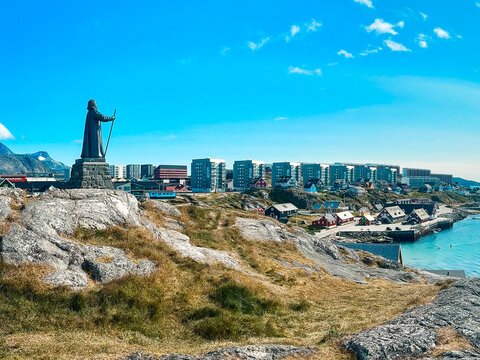 View of the Hans Egede statue on a rocky hill overlooking the colorful buildings and harbor of Nuuk, Greenland.