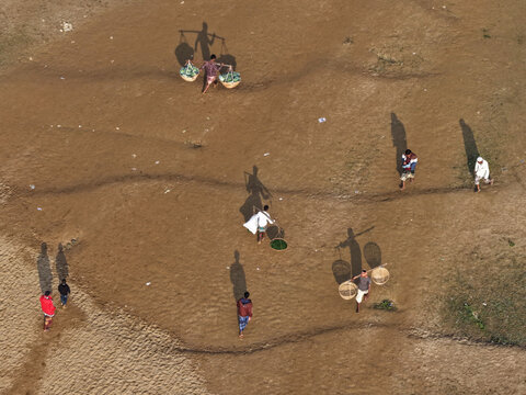 Aerial view of local workers carrying baskets on bamboo poles across a sandy landscape in Sylhet, Sylhet Division, Bangladesh.