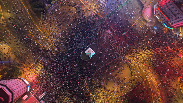 Buenos Aires, Argentina - 19 July 2026: Aerial view of the Obelisco de Buenos Aires surrounded by a massive crowd celebrating at night, with city lights illuminating the urban landscape.
