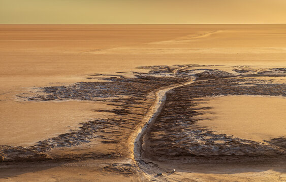 View of the textured salt crust and patterns of Chott el Djerid salt flat under warm golden hour light in Tozeur, Tozeur Governorate, Tunisia.