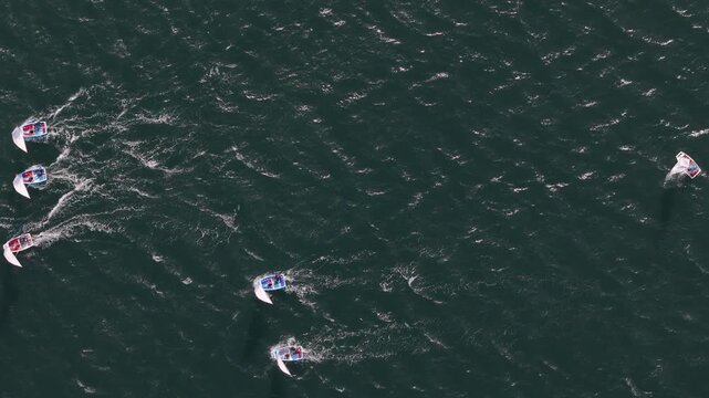 Aerial view of small sailboats racing across the dark blue ocean waters off the coast of Cascais, Lisbon, Portugal.