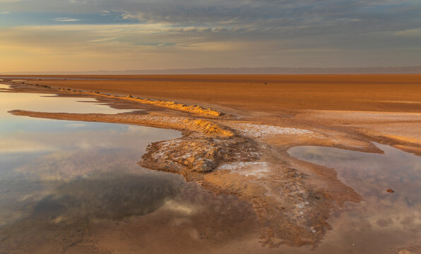 View of the vast salt flats of Chott el Djerid reflecting the golden hour sky with shallow water pools and textured salt crust in Tozeur, Tozeur Governorate, Tunisia.