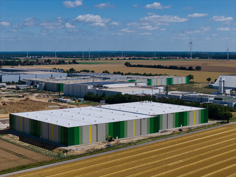Barsinghausen, Lower Saxony, Germany - 08 July 2026: Aerial view of the Gross Munzel industrial warehouse complex with green and white walls, surrounded by agricultural fields and wind turbines.
