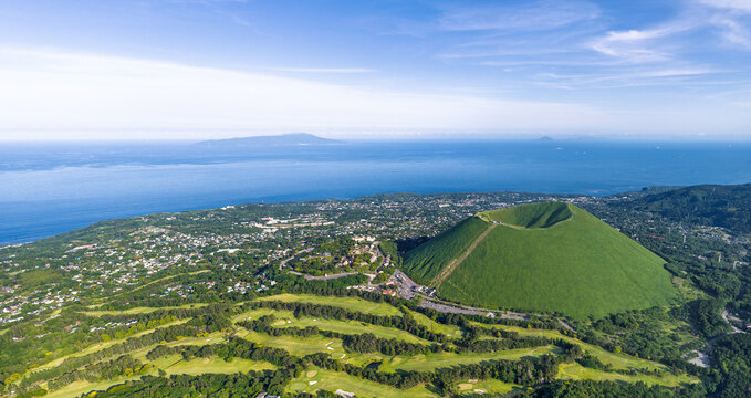 Aerial view of Mt. Omuro, a dormant volcanic cone with a lush green crater, surrounded by golf courses and the coastal town of Ito, Shizuoka, Japan.